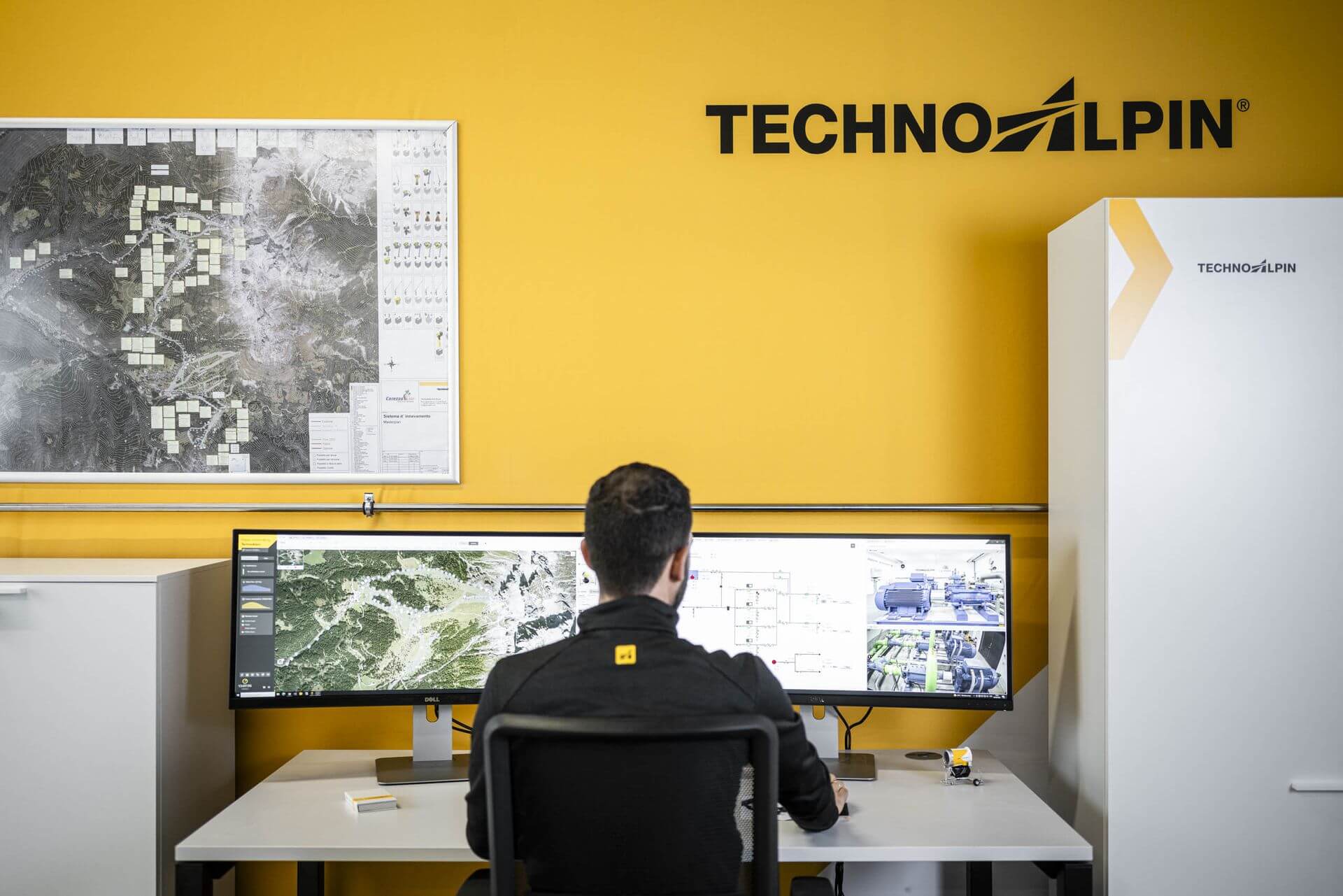 An employee of TechnoAlpin at a desk in front of two screens