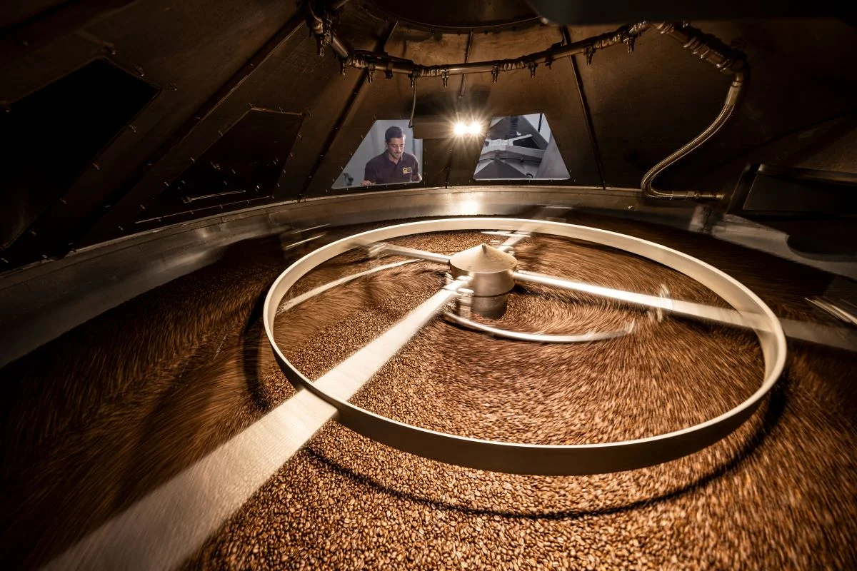 Kaffeebohnen kühlen und rotieren in einer Röstmaschine unter warmem industriellem Licht.