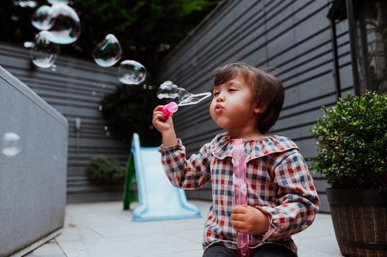 A little girl sitting in a garden blowing bubbles