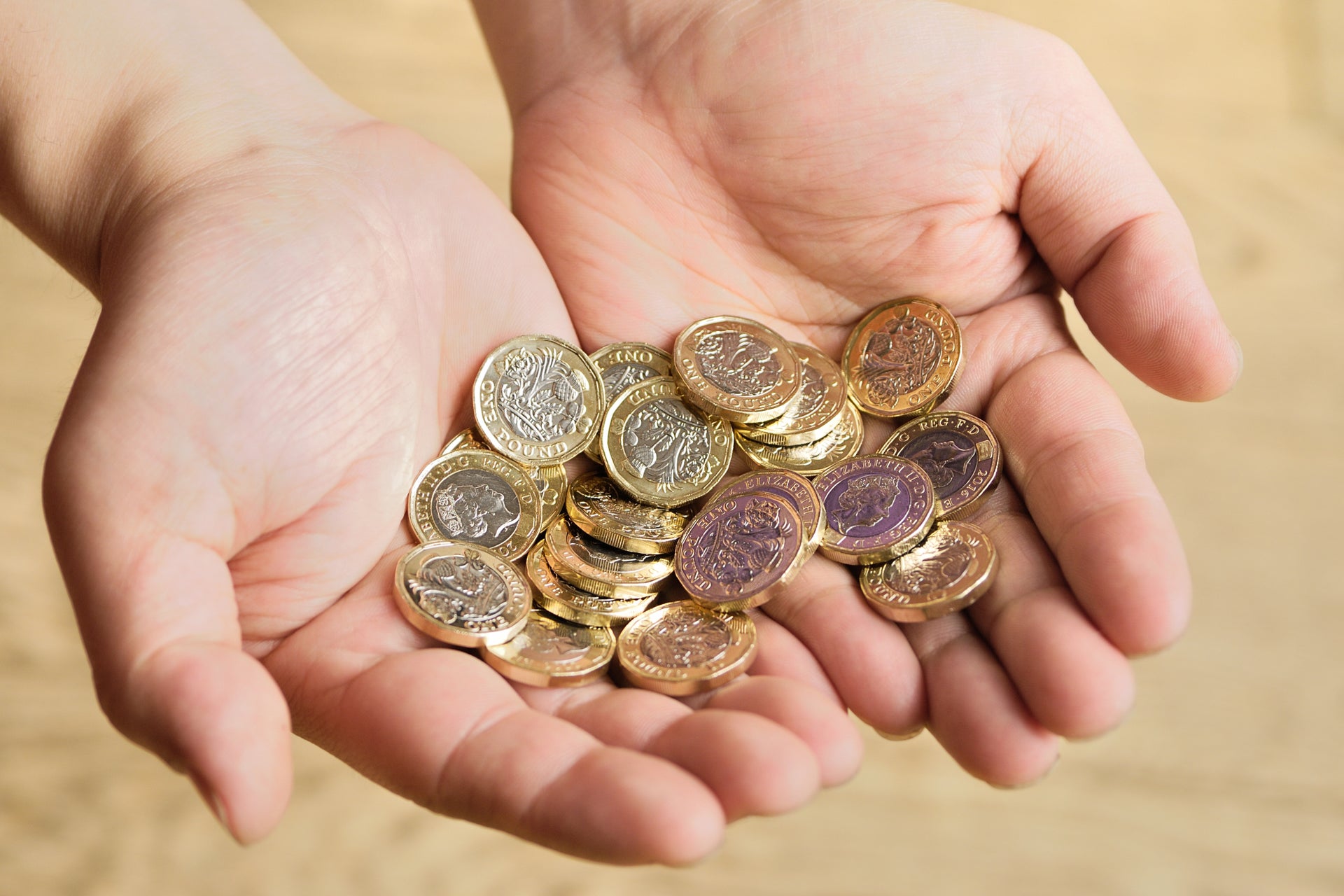 Two hands holding a collection of pound coins