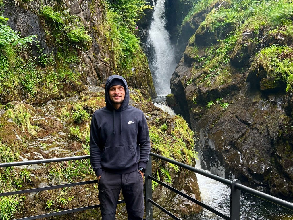 Man in a sweatshirt standing in front of a waterfall Man in a sweatshirt standing in front of a waterfall
