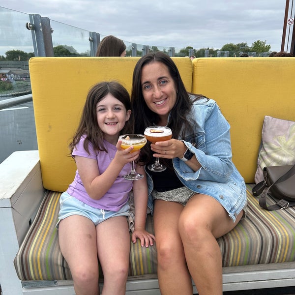 Little Girl and her mum sitting outside on a couch. They are "cheers"ing their drinks and smiling. Little Girl and her mum sitting outside on a couch. They are "cheers"ing their drinks and smiling.