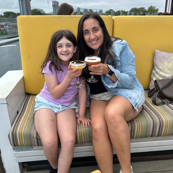 Little Girl and her mum sitting outside on a couch.  They are "cheers"ing their drinks and smiling.  Little Girl and her mum sitting outside on a couch.  They are "cheers"ing their drinks and smiling.