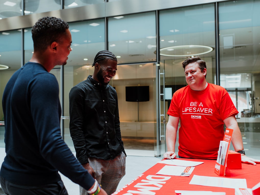 Three men gathered around a table, one wearing a DKMS t-shirt Three men gathered around a table, one wearing a DKMS t-shirt