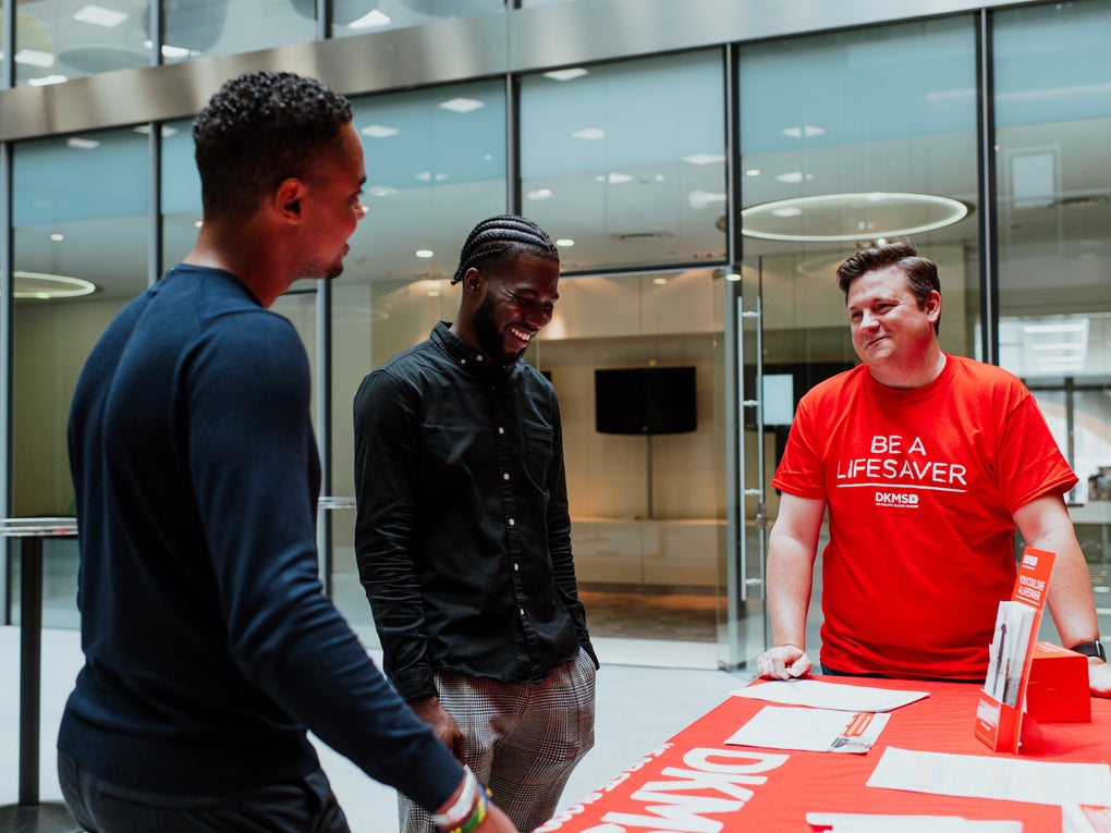 Three men gathered around a table, one wearing a DKMS t-shirt Three men gathered around a table, one wearing a DKMS t-shirt