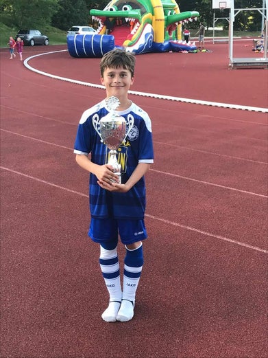 Mattes is holding a trophy wearing a blue and white football kit he is looking straight into the camera