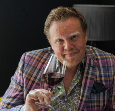 Image of Olly Smith holding a glass of wine smiling into the camera