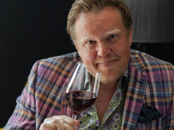 Image of Olly Smith holding a glass of wine smiling into the camera
