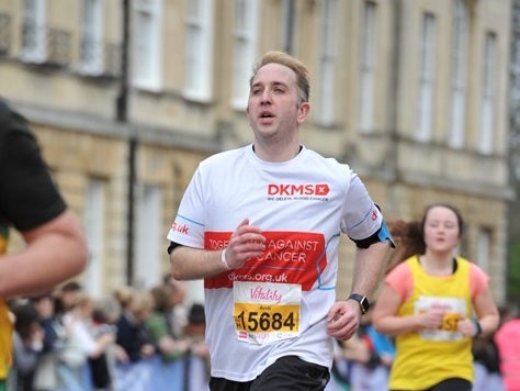 Man wearing DKMS Top runs in a race, with other runners and supporters in the background. Man wearing DKMS Top runs in a race, with other runners and supporters in the background.