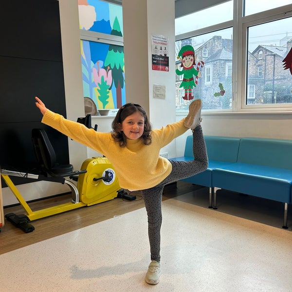 A little Girl dances in a waiting area.  She is smiling and standing on one leg.  A little Girl dances in a waiting area.  She is smiling and standing on one leg.