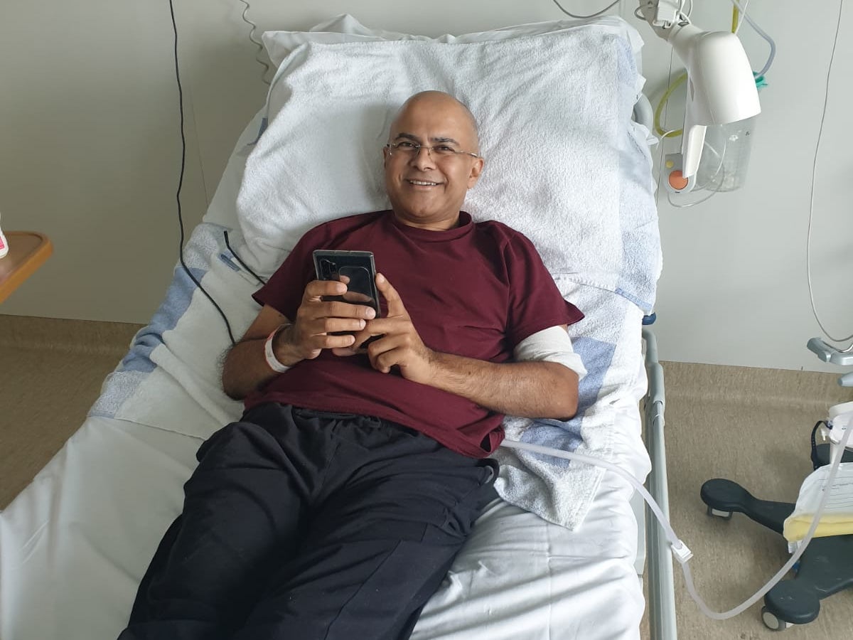 Rakesh laying in a hospital bed, smiling at the camera.