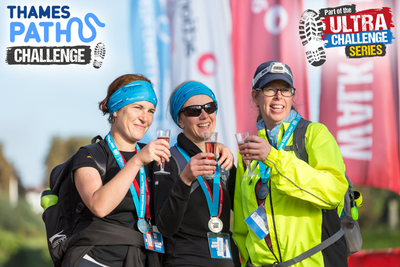 Three women with glasses of fizz at the finish line of the Thames Path Challenge