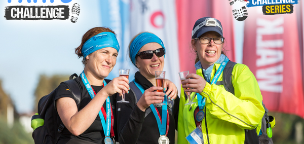 Three women with glasses of fizz at the finish line of the Thames Path Challenge