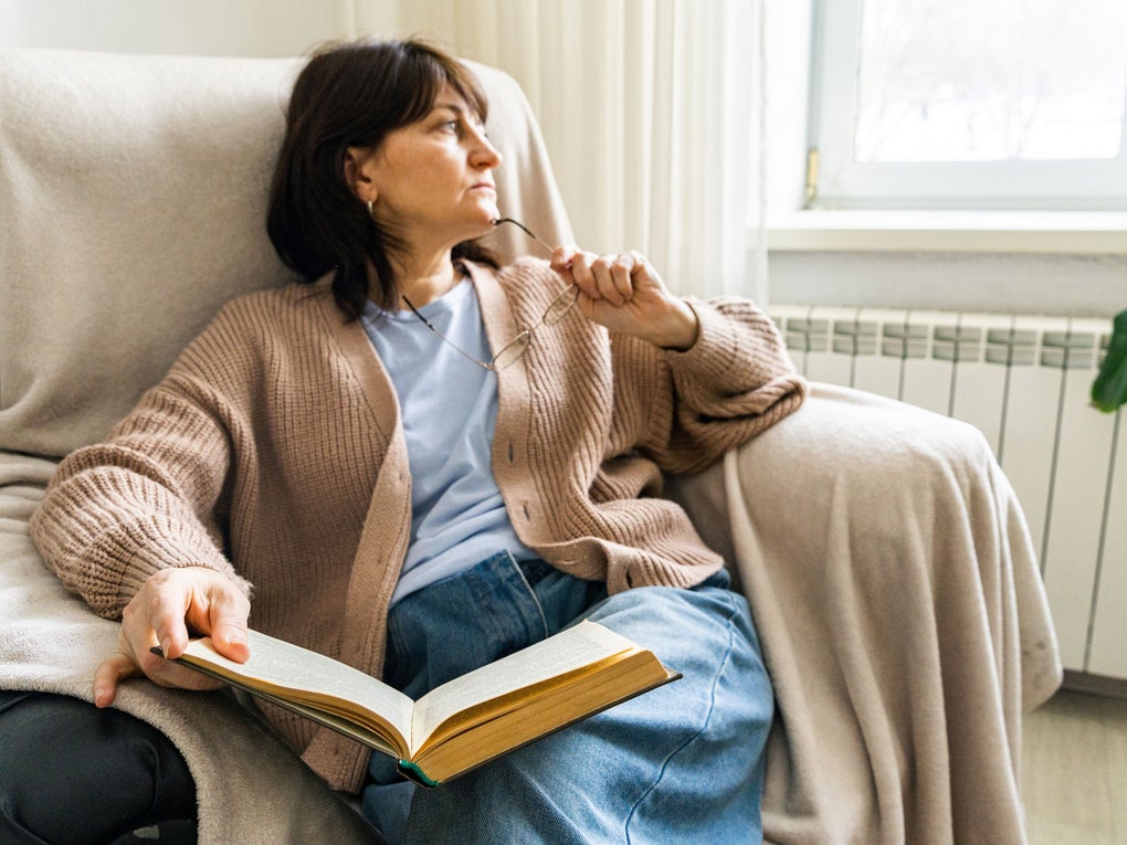Woman with book sitting in armchair thinking about something and contemplating it Woman with book sitting in armchair thinking about something and contemplating it