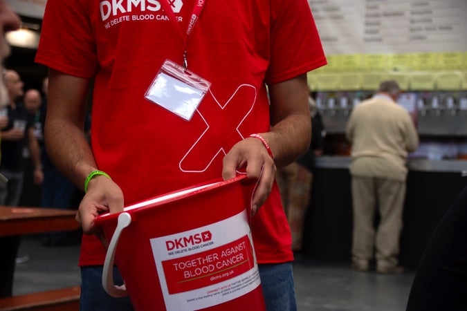 DKMS volunteer in red DKMS tshirt holding a fundraising bucket