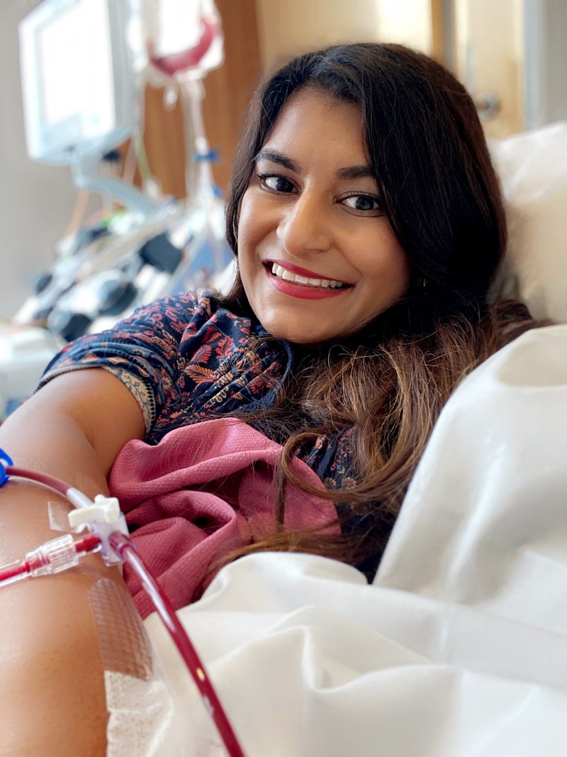 Poonam in a hospital bed, smiling at the camera whilst donating blood stem cells