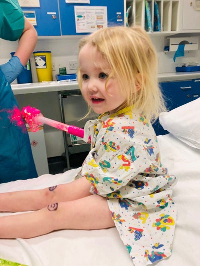 Josie sittingon a hospital bed with smily faces drawn on her knees Josie sittingon a hospital bed with smily faces drawn on her knees