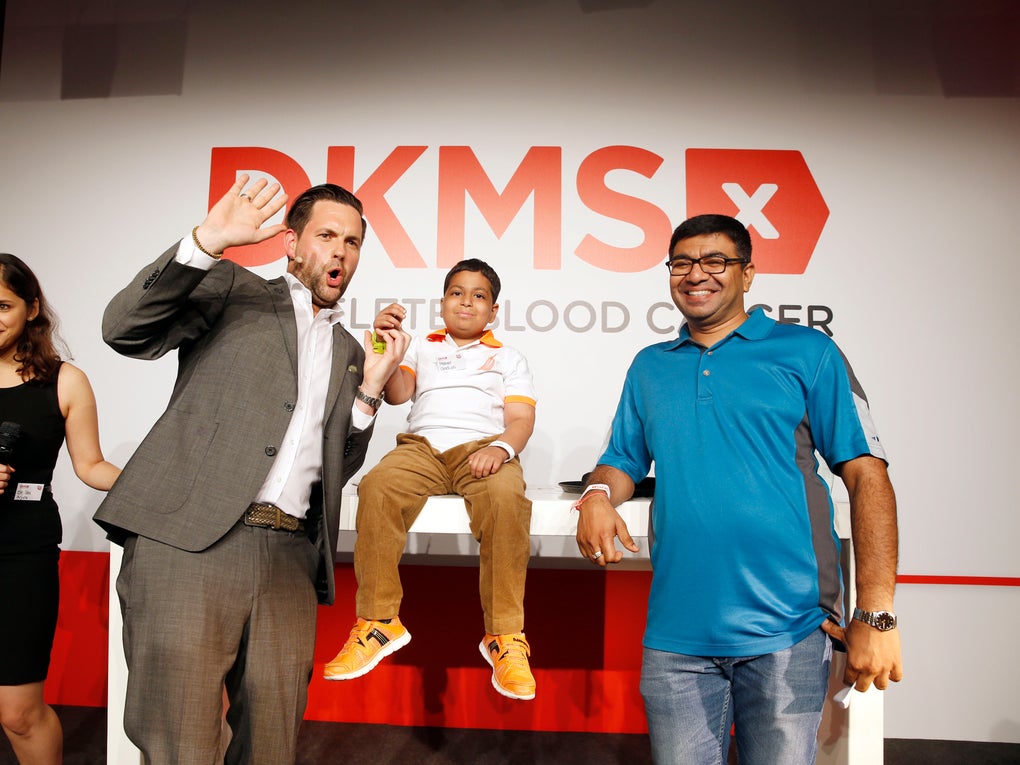 Four people in front of the DKMS logo smiling and cheering Four people in front of the DKMS logo smiling and cheering