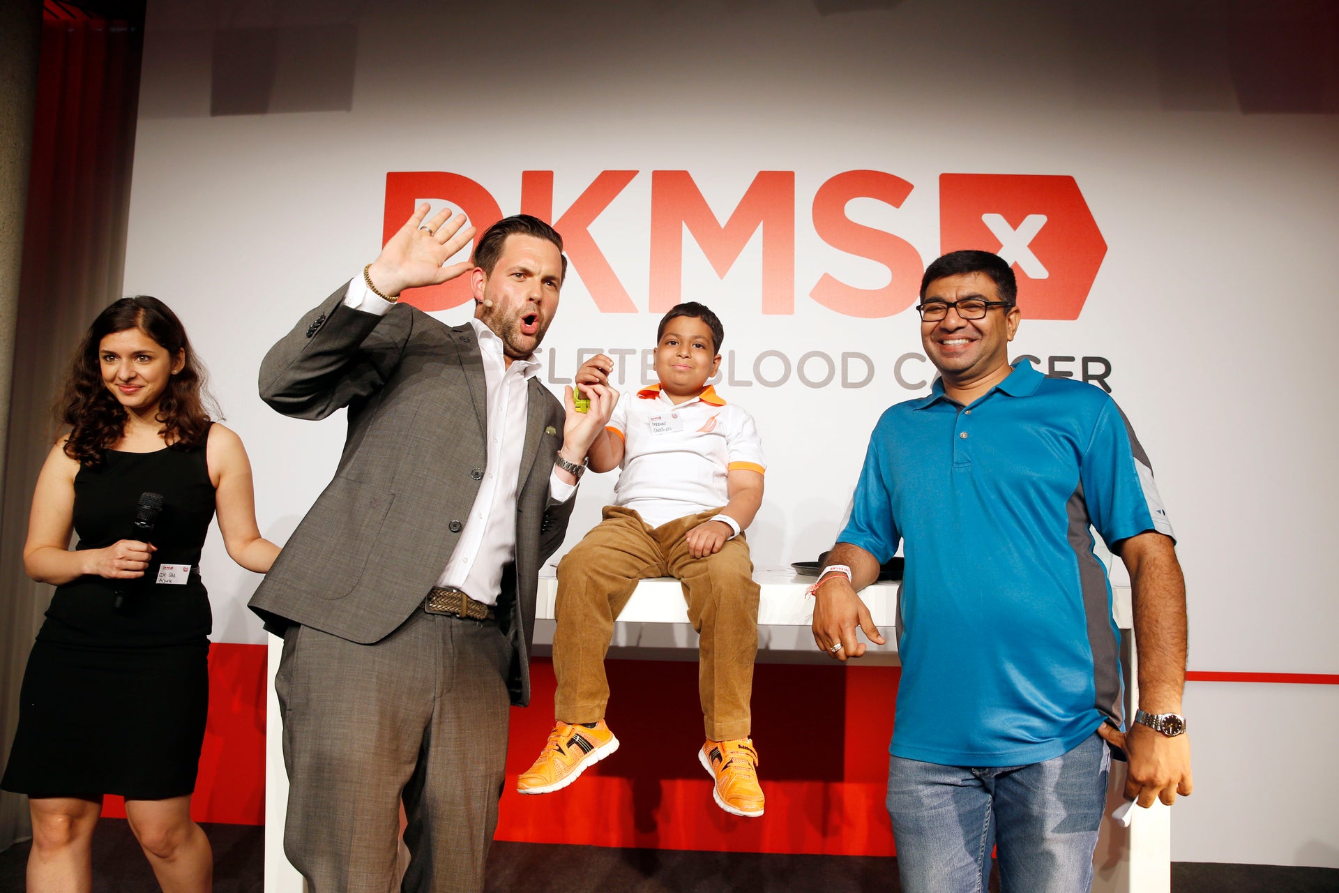Four people in front of the DKMS logo smiling and cheering
