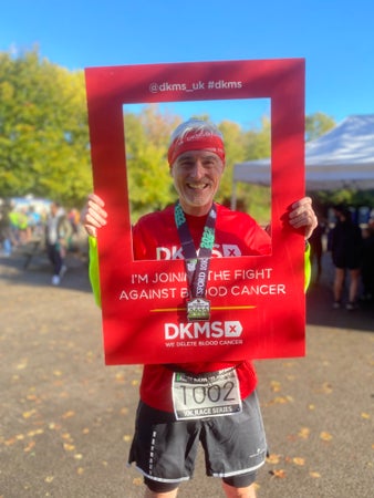 Runner at a fundraising event wearing a medal and holding a DKMS 'I'm joining the fight against blood cancer' banner