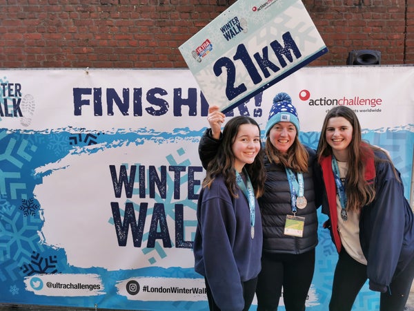 Three women wearing medals holding a 21km sign at the end of the Winter Walk.