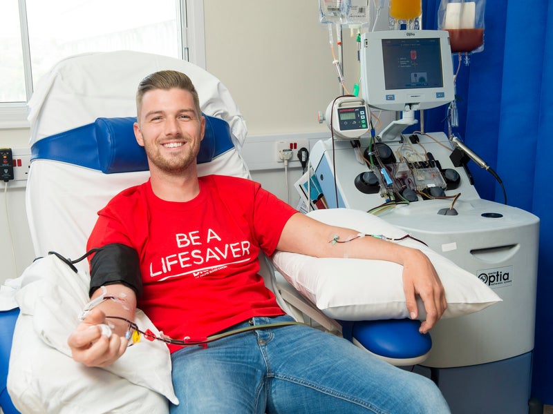 Person in a hospital chair, wearing a DKMS t-shirt, donating blood stem cells. 