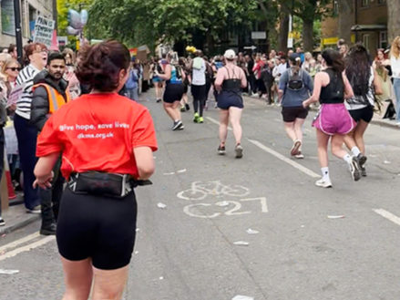 Girl wearing DKMS Running top runs in Half marathon, with other runners and supporters in the background Girl wearing DKMS Running top runs in Half marathon, with other runners and supporters in the background
