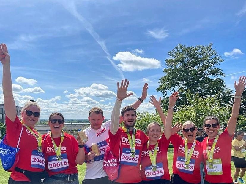 Group of runners stand on grass, holding their hands up in celebration, while wearing Red DKMS tops and race medals. Group of runners stand on grass, holding their hands up in celebration, while wearing Red DKMS tops and race medals.