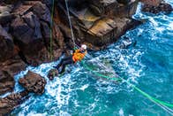Climber crossing a Tyrolean Traverse rigged above the sea, Cruit Island, County Donegal
