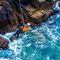 Climber crossing a Tyrolean Traverse rigged above the sea, Cruit Island, County Donegal