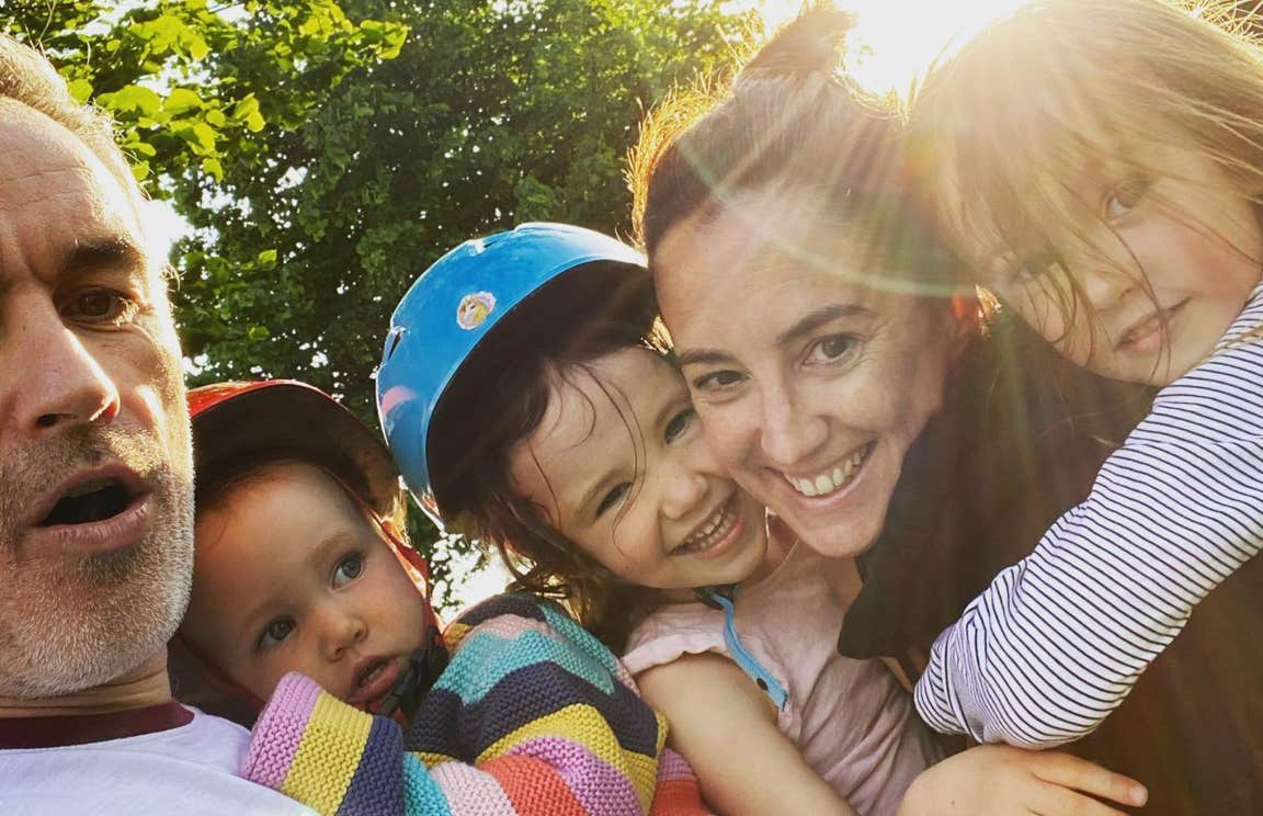 A family smiling at the camera with the sun shining behind them.
