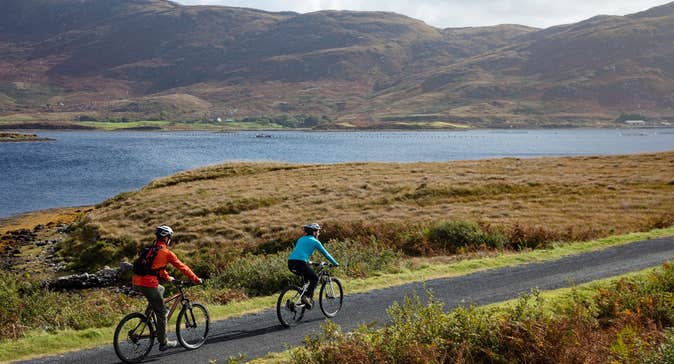 Two people cycling on a laneway beside the water.