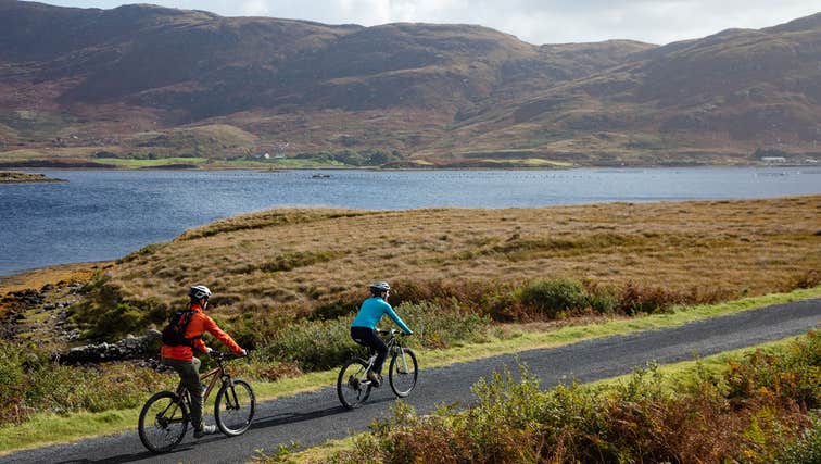 Two people cycling on a laneway beside the water.