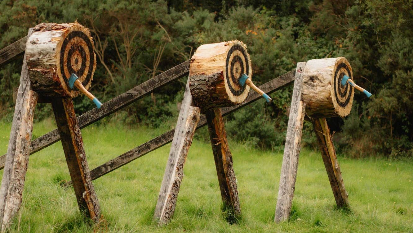 Three wooden targets in a field with an axe in the middle of each
