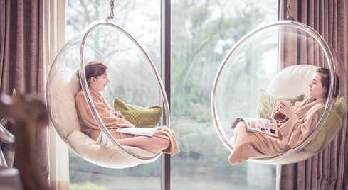 Two friends sitting in hanging chairs at a spa.