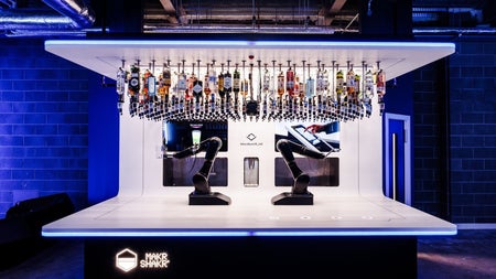Two robotic arms under optics holding bottles of spirits