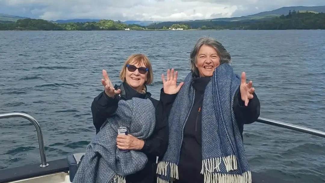 Two people smiling on a boat with the sea and mountains in the background