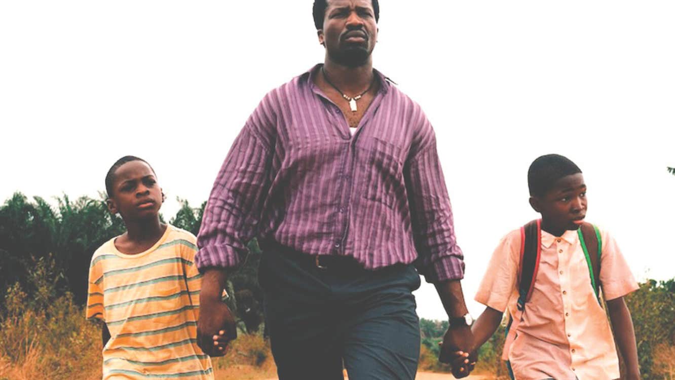 A determined looking man is walking along a road holding the hand of 2 young boys either side of him.