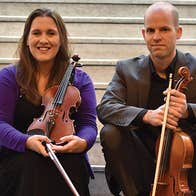 Smiling group of 4 seated on stone steps holding violins