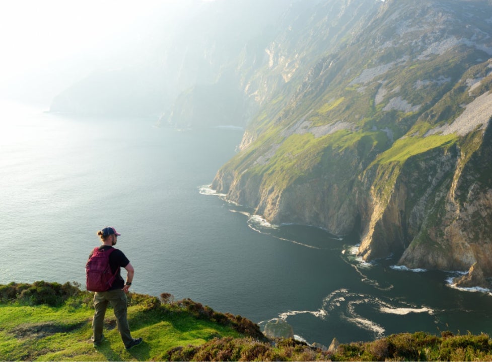 A person standing on a cliff edge looking out and very high sea cliffs