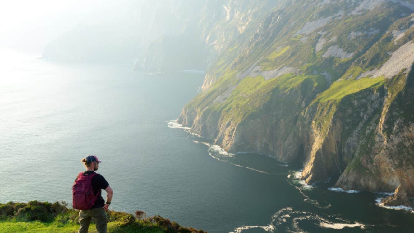 A person standing on a cliff edge looking out and very high sea cliffs