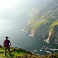 A person standing on a cliff edge looking out and very high sea cliffs