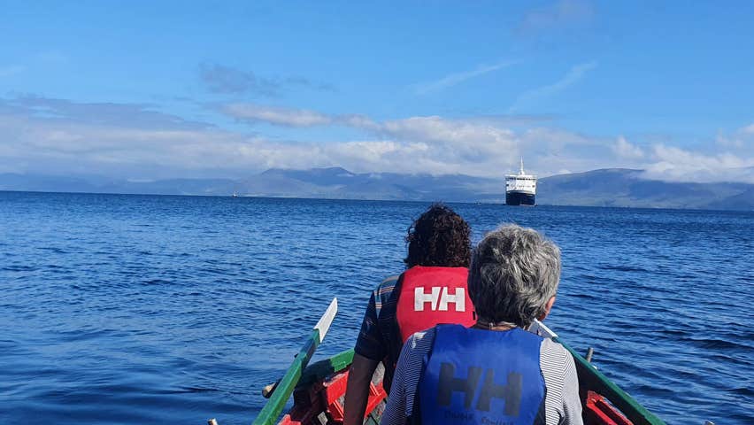 Two ladies in a rowing looking at a cruise ship in the bay