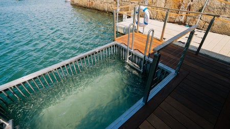 Enclosed sea plunge pool with steps and railing set on a harbour dock beside stone walls