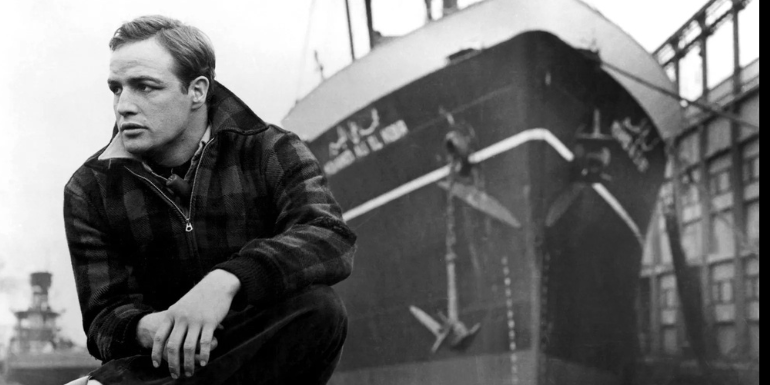A young Marlon Brando is sitting in front of a ship.