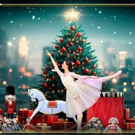 A woman in white dress is standing on one leg in ballet pose with other leg and arm outstretched, with christmas tree and toys behind.