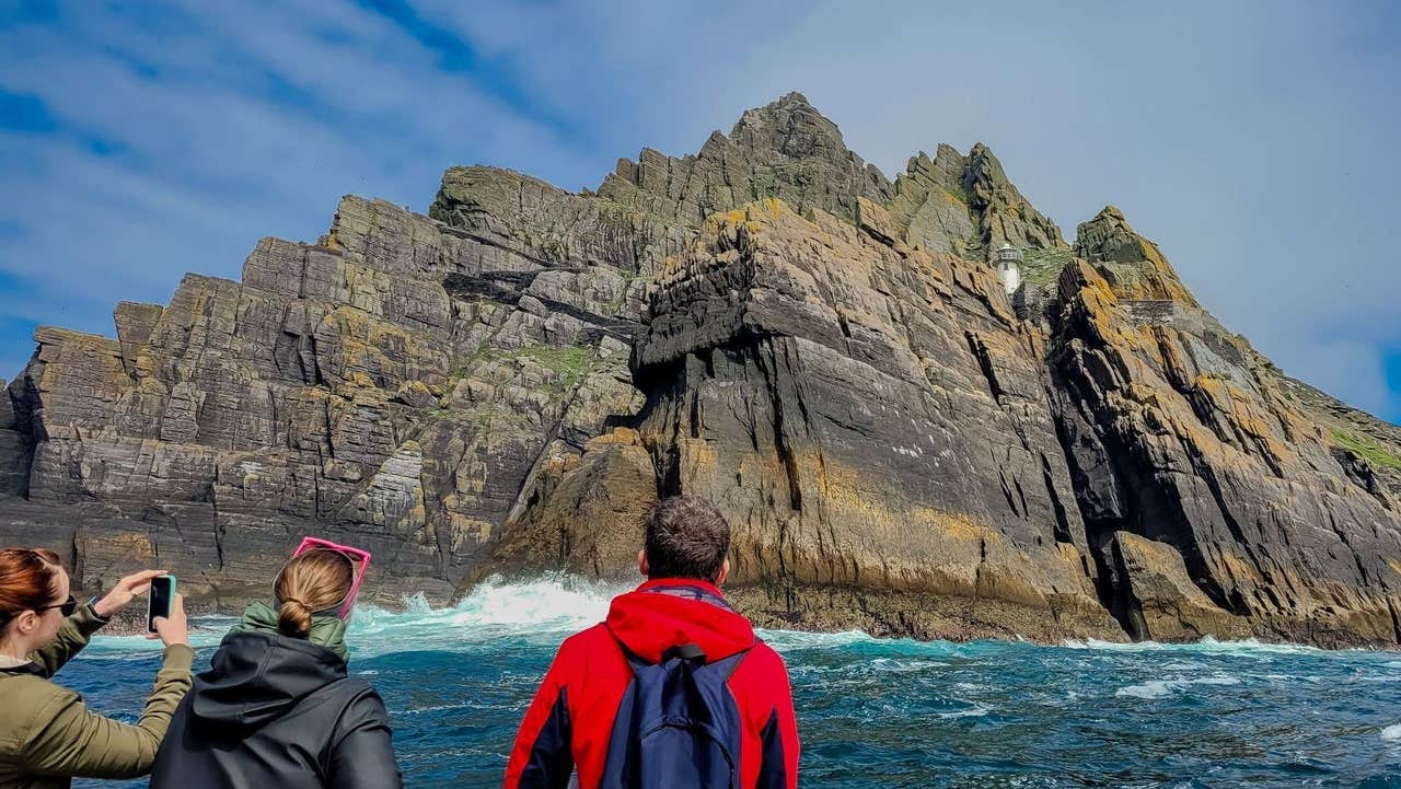 Three passengers on a tour boat taking photos of Small Skellig island
