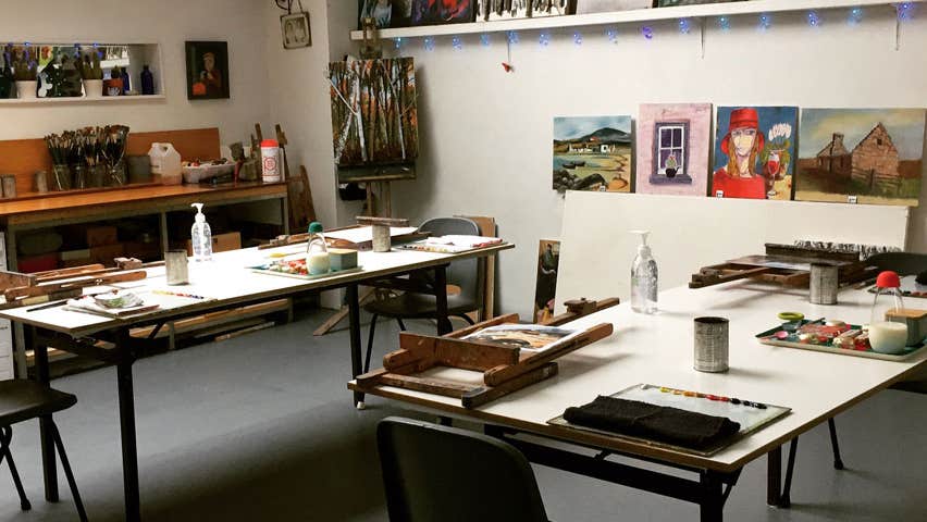 A view of the interior of the studio classroom with various painting materials on the tables and paintings on display on the walls