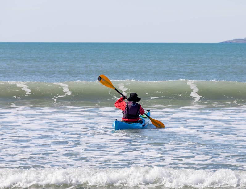 Pictures a sea-kayaker, paddling towards a coming wave on Garrylucas Beach, Kinsale.