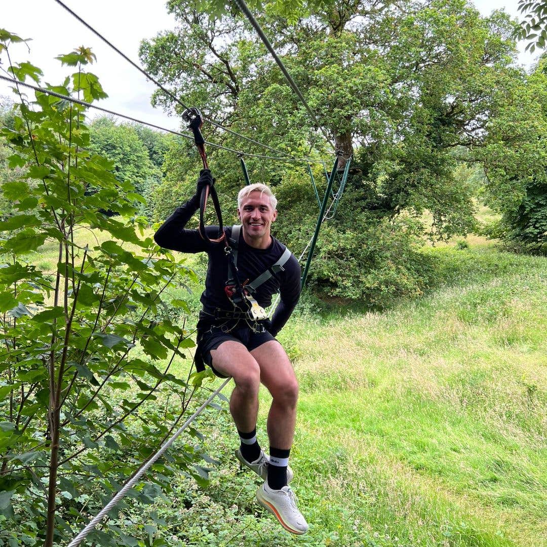 Man sitting in a harness on a zipline in an adventure park.